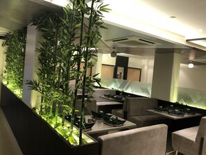 A modern restaurant interior with bamboo plants, cushioned seating, and a long dining table. - Kyriad Hotel Vijayapura (Bijapur)