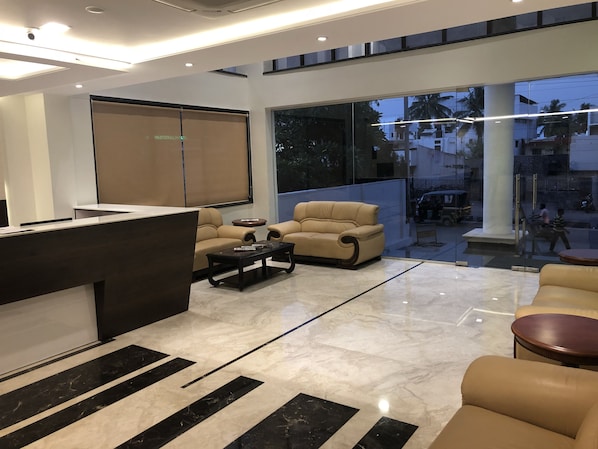 A modern lobby with a reception desk, two sofas, a coffee table, and large windows offering a view of the street.