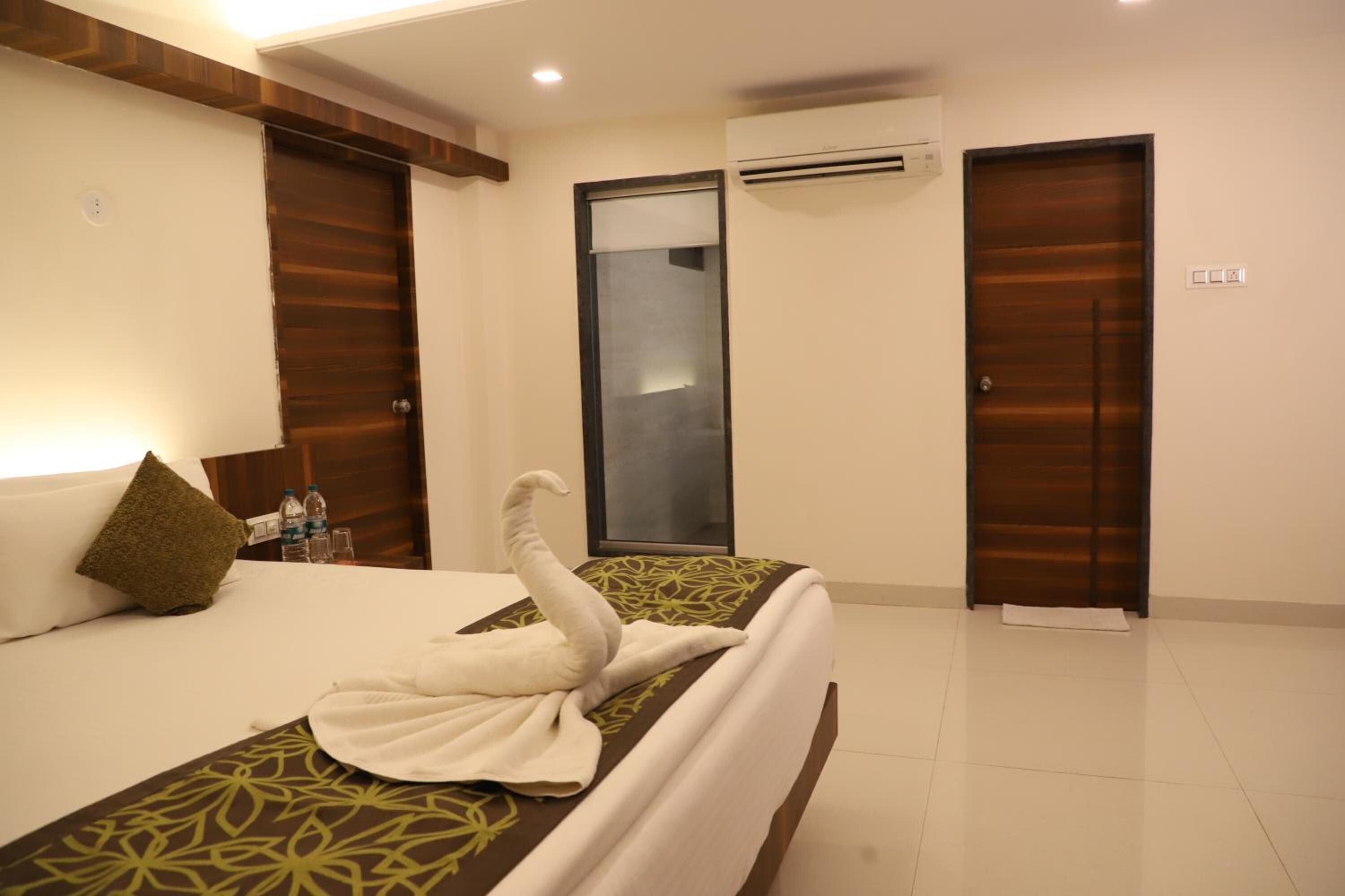 A hotel room with a bed, a wall-mounted air conditioner, and two doors.