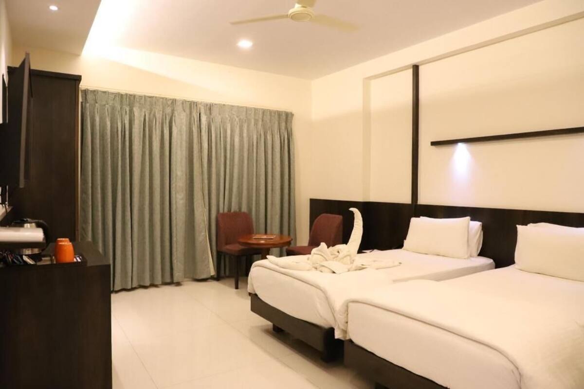 A hotel room with a bed, two chairs, a desk, a television, and a ceiling fan.