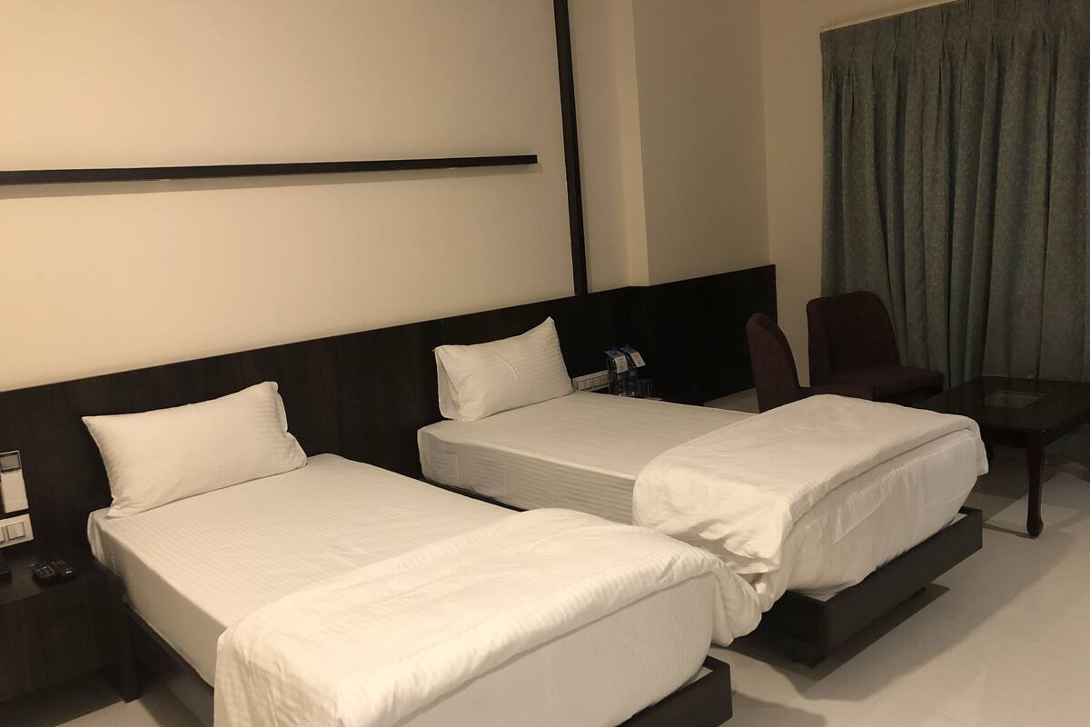 A hotel room with two single beds, a nightstand, a chair, and a table.