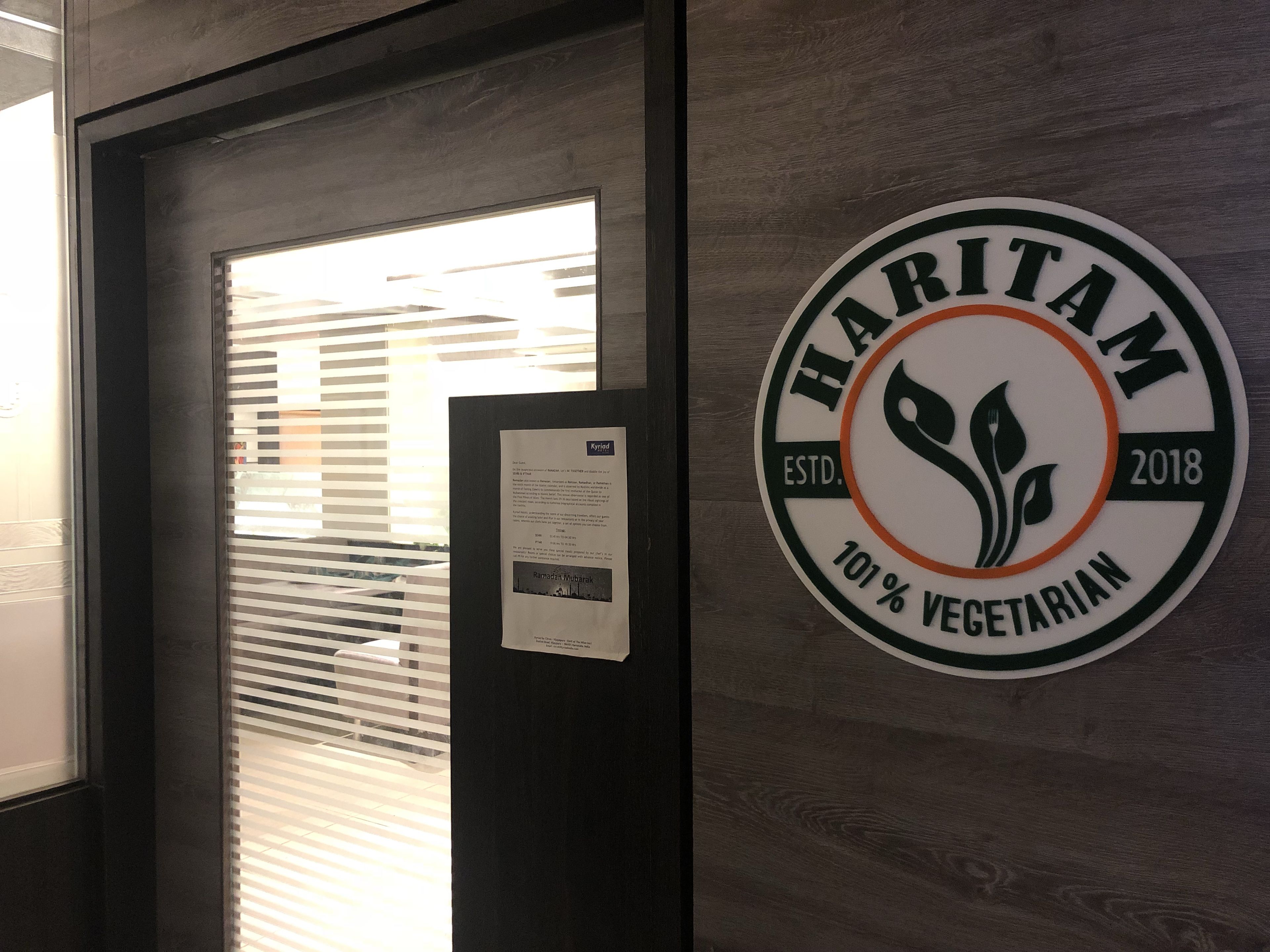 A Haritam sign on a wall with a window and blinds in the background.