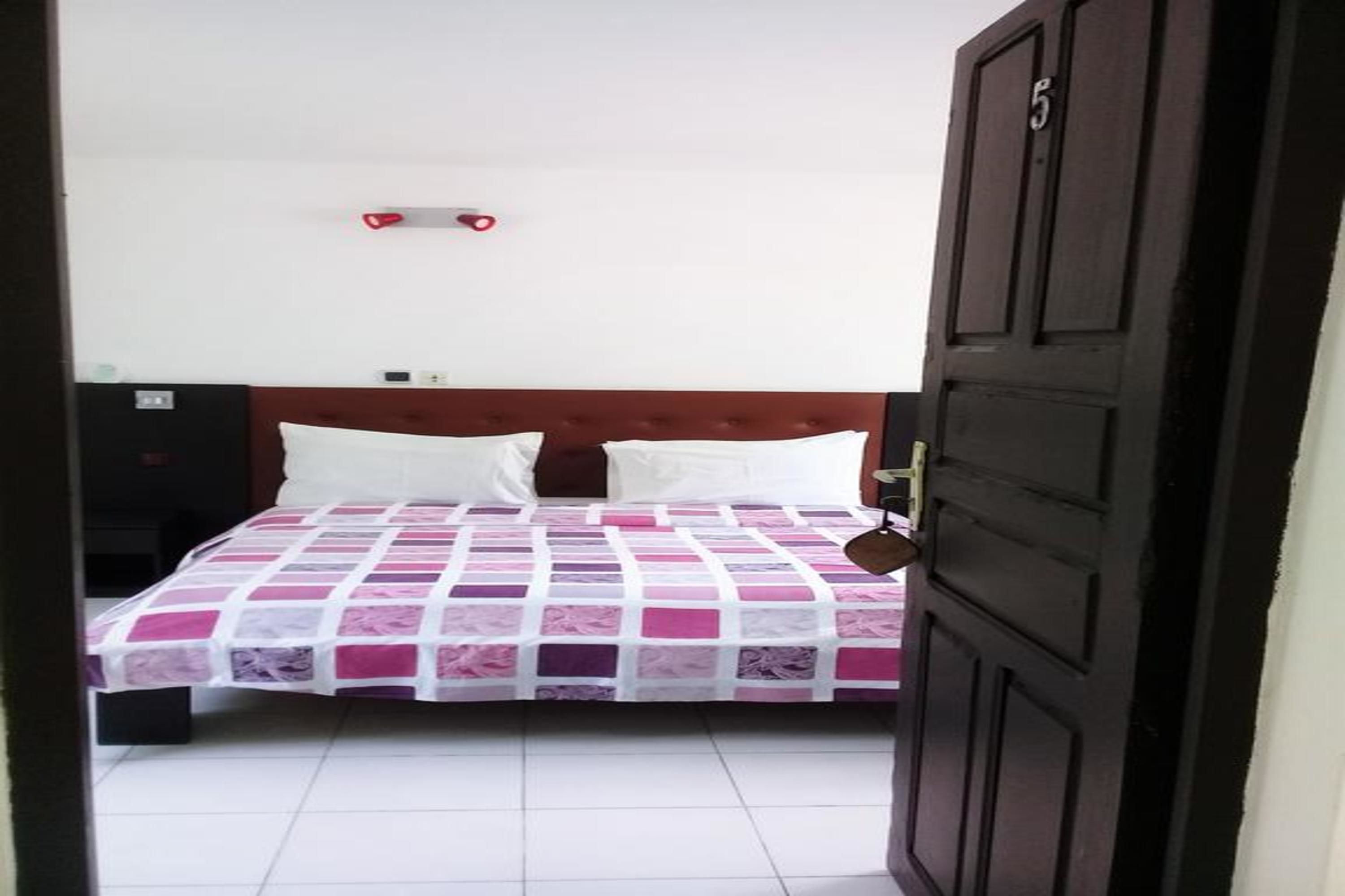 A bedroom with a bed, white pillows, a red headboard, and a door.