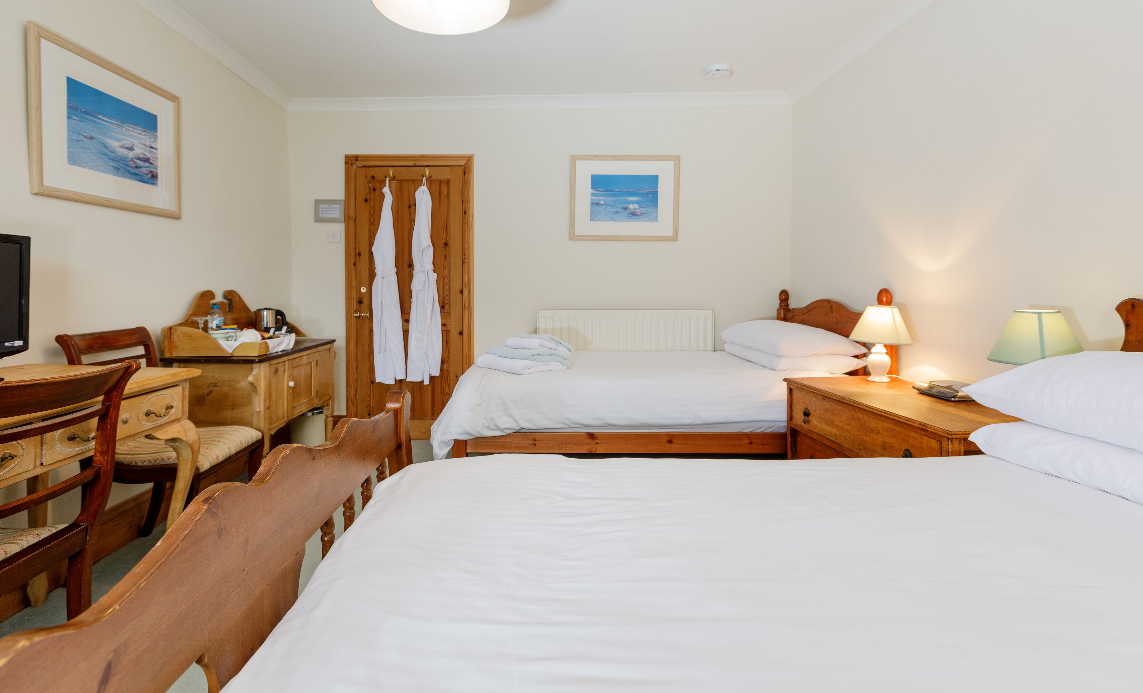 A hotel room with two beds, a wooden desk, a chair, and a television.