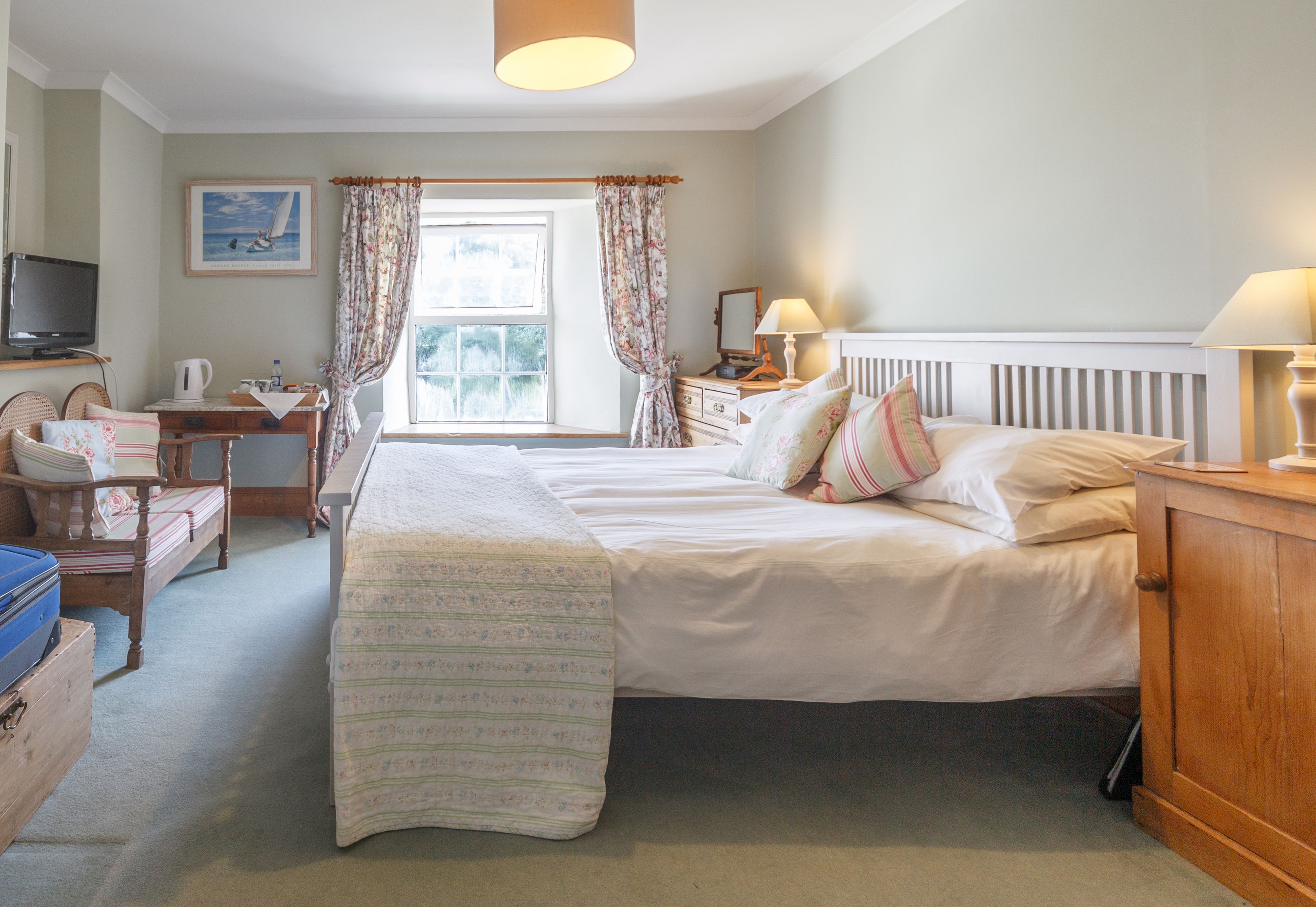 A bedroom with a large bed, a desk with a lamp, a television, and a window with curtains.