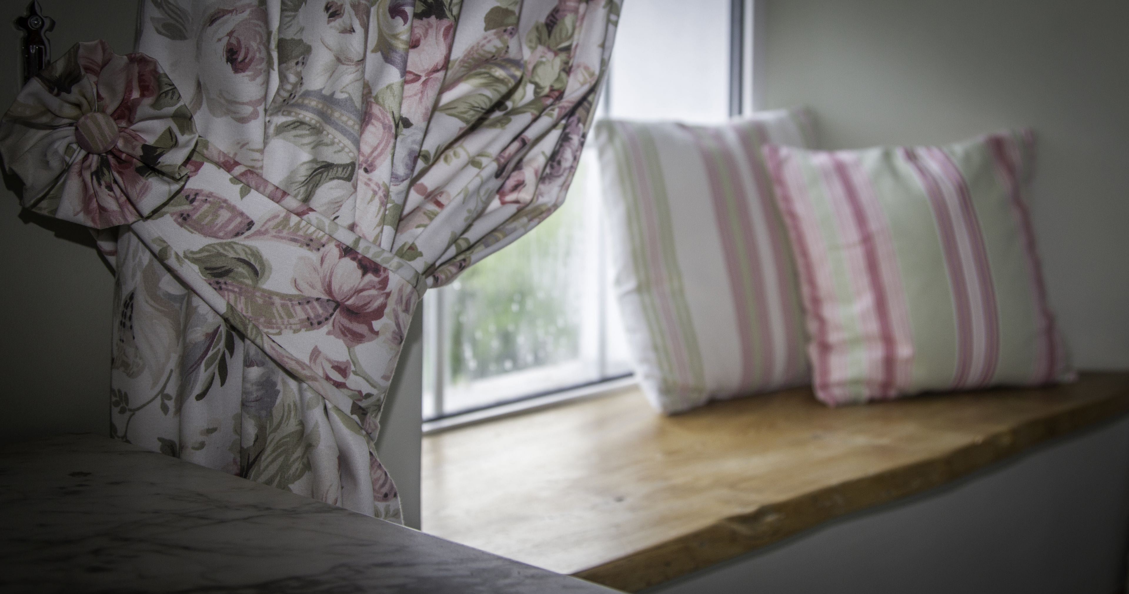 A bed with floral-patterned curtains, a wooden headboard, and striped pillows on a window sill.