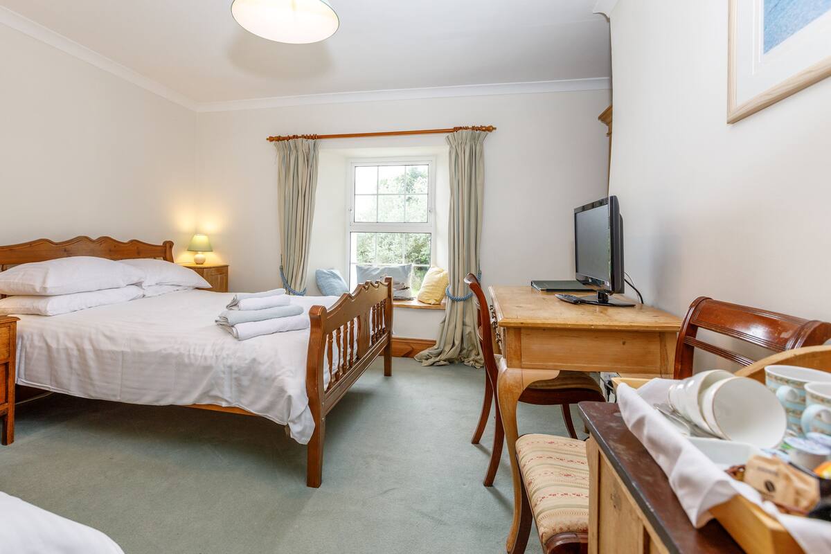 Une chambre d’hôtel comprenant un lit, une table de chevet avec une lampe, un bureau avec un ordinateur, une chaise et une fenêtre avec des rideaux.