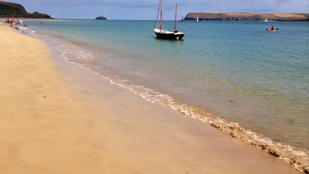 A sandy beach with calm waters, a sailboat, and a distant sailboat on the horizon. - Treweens Bed & Breakfast (Wadebridge)