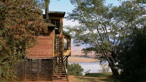 A wooden cabin with a balcony, surrounded by trees and a lake view. - Treks Trips and Trails (Cathkin Park)