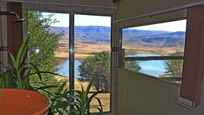 A room with a large sliding glass door leading to a scenic view of a river and mountains. - Treks Trips and Trails (Cathkin Park)