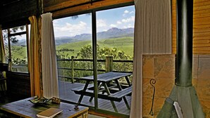 A rustic cabin with a wooden deck, a stone fireplace, and a view of rolling hills. - Treks Trips and Trails (Cathkin Park)