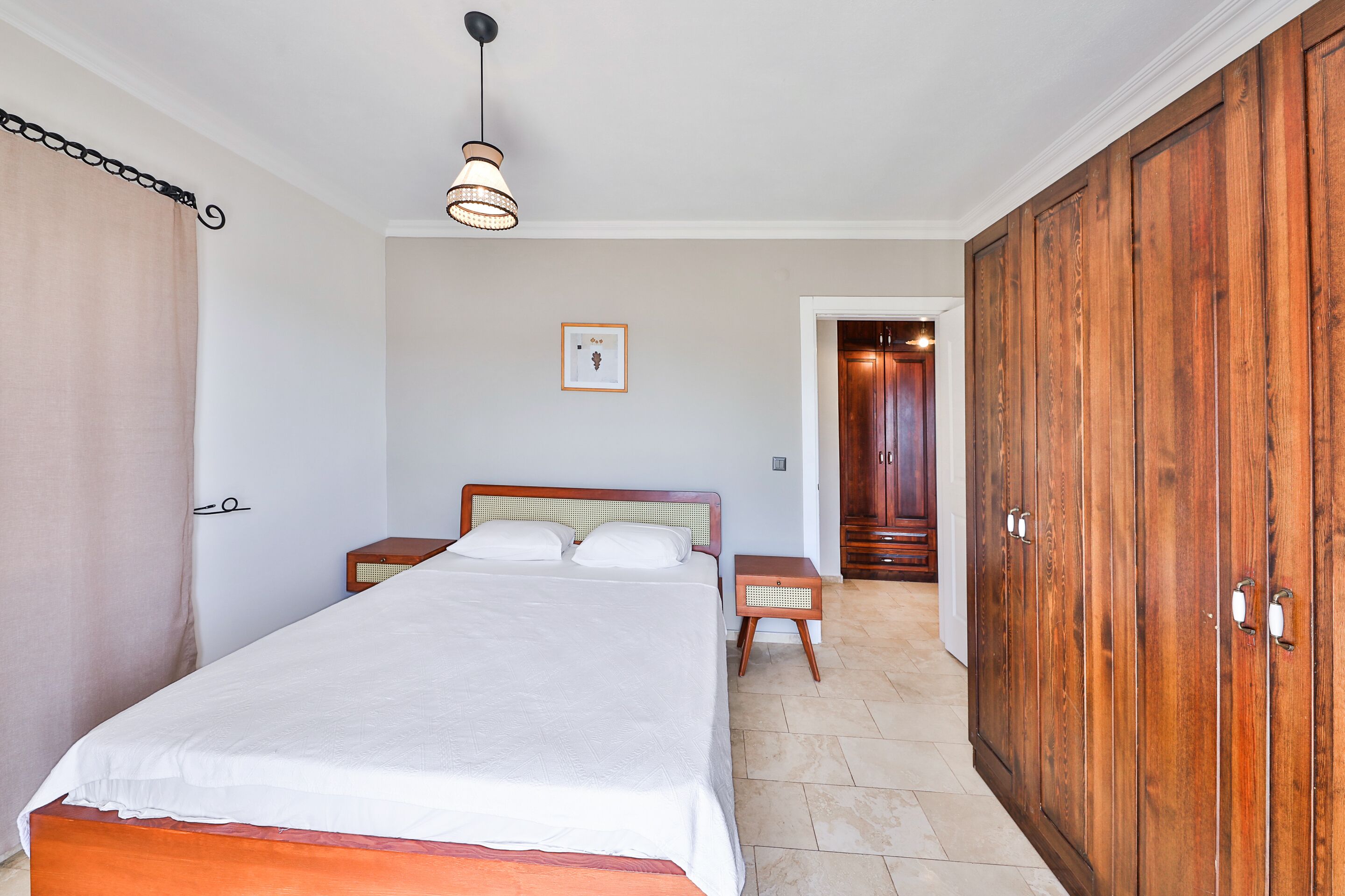 Une chambre à coucher comprenant un lit, des tables de chevet, une armoire et un luminaire suspendu.