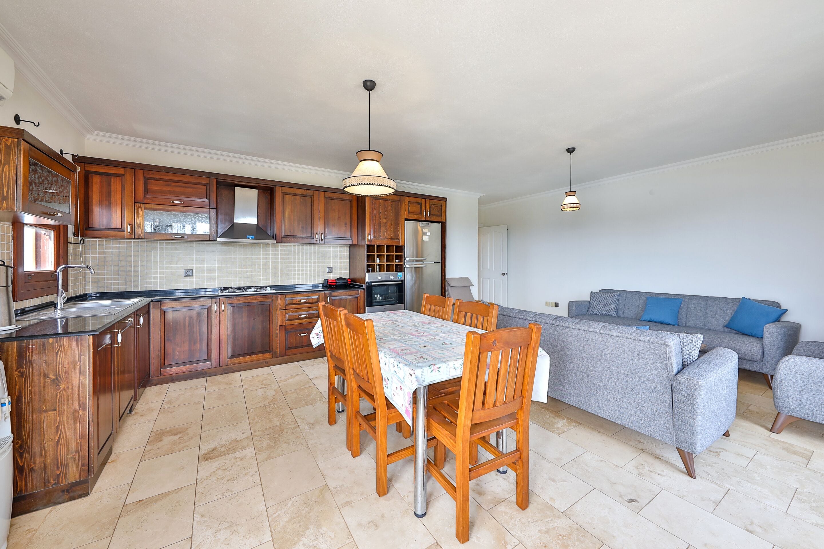 A modern kitchen with wooden cabinets, a dining table with chairs, and a grey sofa.
