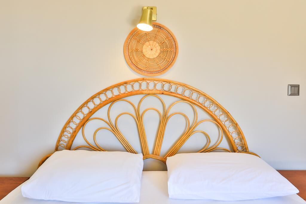 A bed with a woven headboard and two white pillows, a wall-mounted light fixture, and a small electrical outlet.