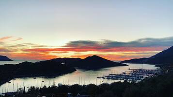 Un port de plaisance avec des bateaux amarrés, entouré de collines et illuminé par un coucher de soleil.