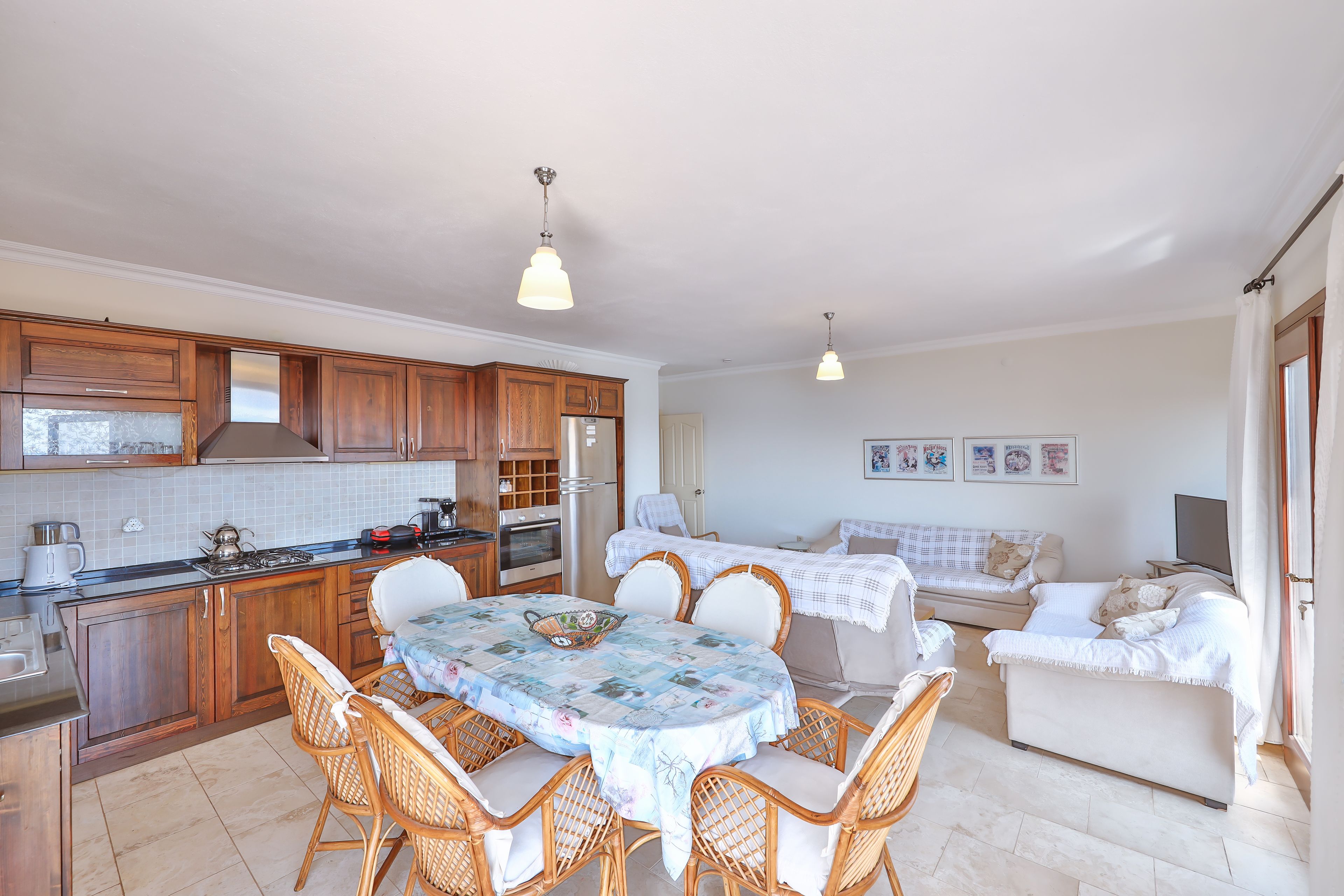 A kitchen with wooden cabinets, a dining table with chairs, and a sofa in the living area.