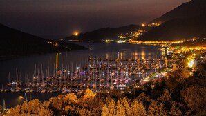 Un port de plaisance la nuit, avec des bateaux amarrés, entouré de collines et illuminé par les lumières de la ville.