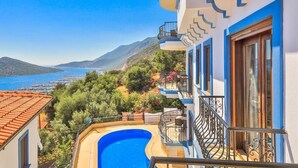 Un bâtiment doté d’une piscine à bords incurvés, d’un balcon avec une balustrade et offrant une vue sur la mer et les montagnes.