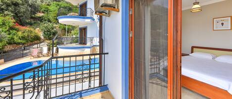En balkon med swimmingpool, seng og udsigt over et bjergrigt landskab.