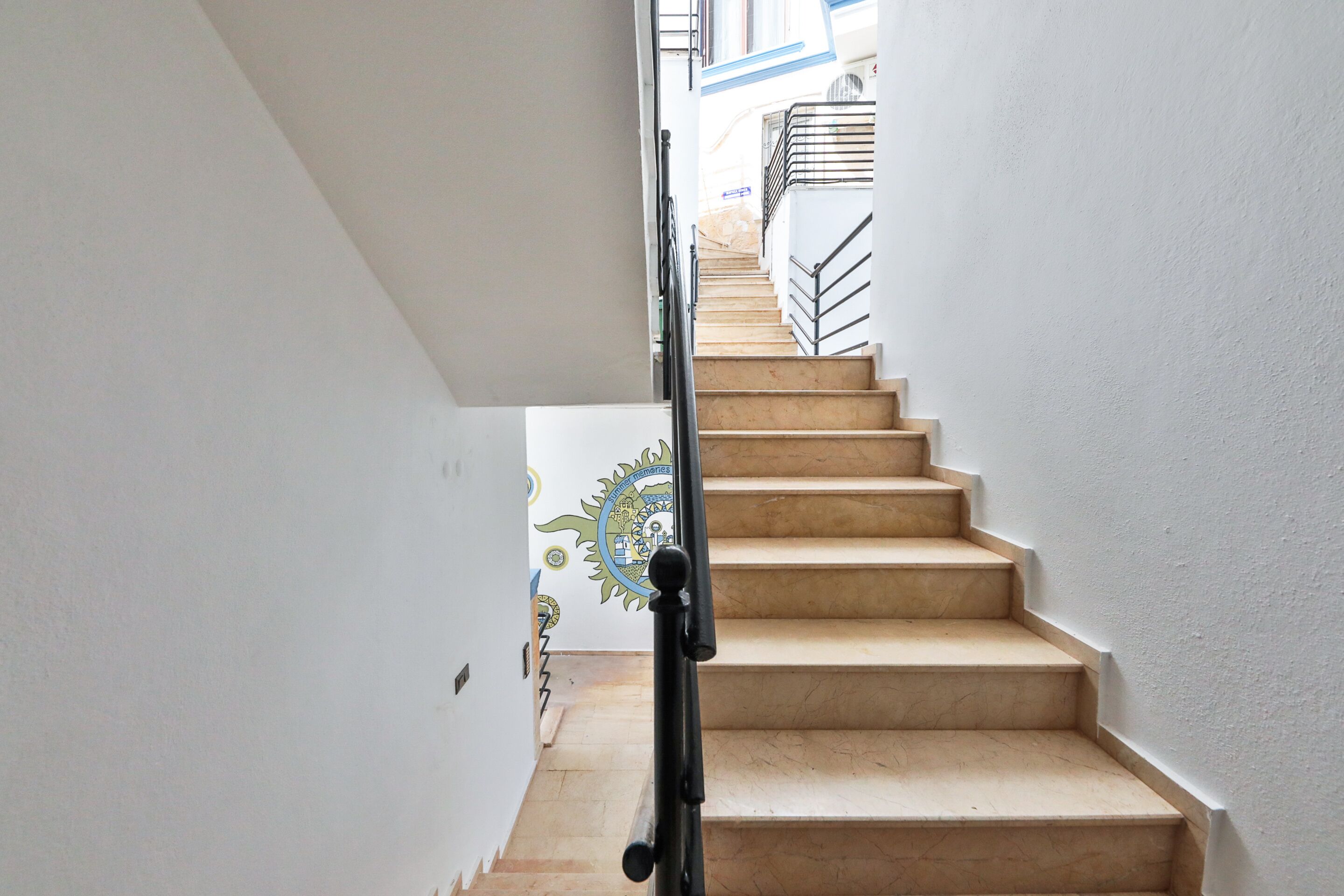 A staircase with beige steps and a black handrail, leading to an upper floor.