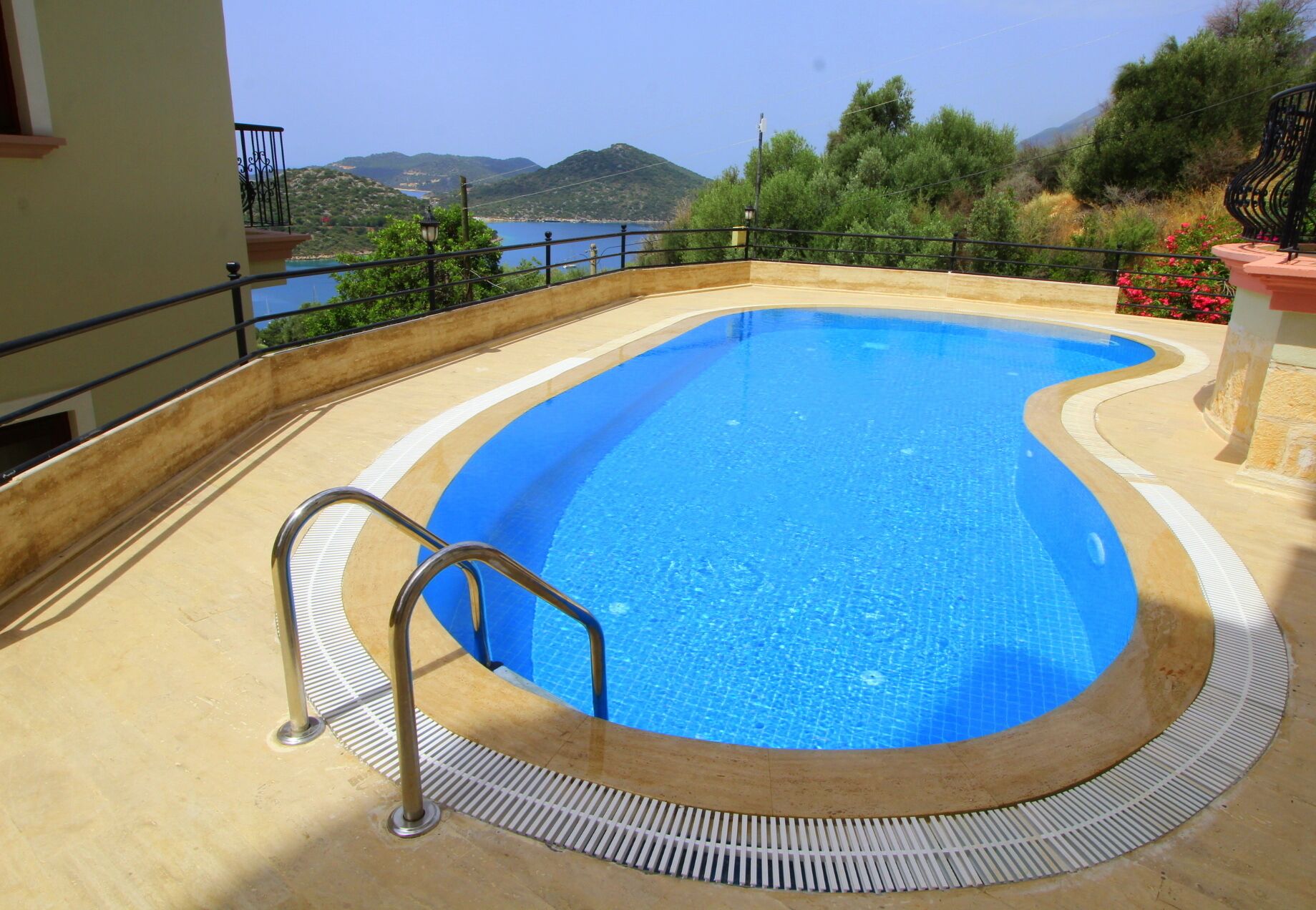 Une piscine à bord incurvé, une échelle en métal et une vue sur la mer et les collines en arrière-plan.