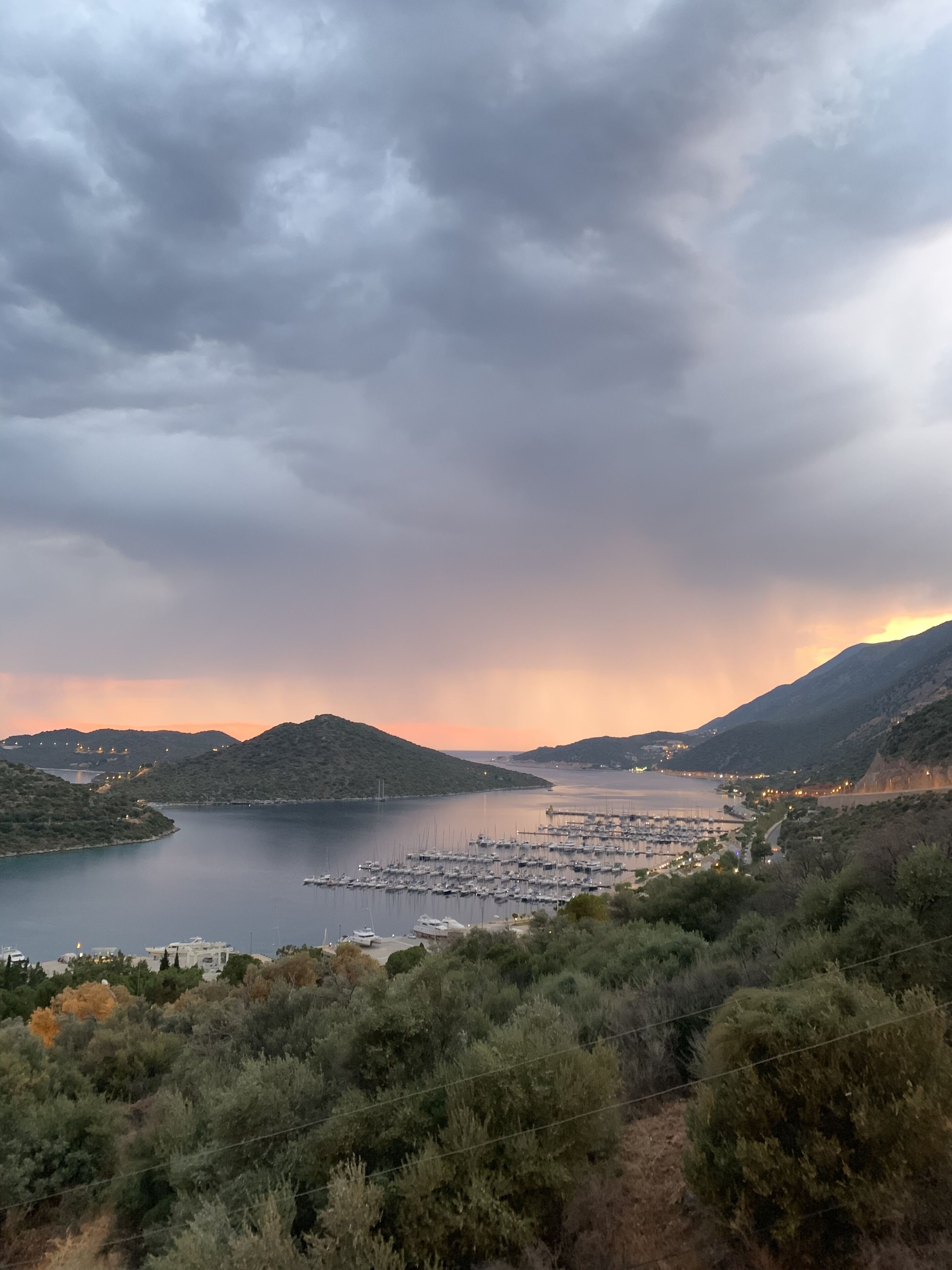 Eine Küstenlandschaft mit einem Hafen, Hügeln und einem Sonnenuntergang.