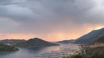 Eine Küstenlandschaft mit einem Hafen, Hügeln und einem Sonnenuntergang.