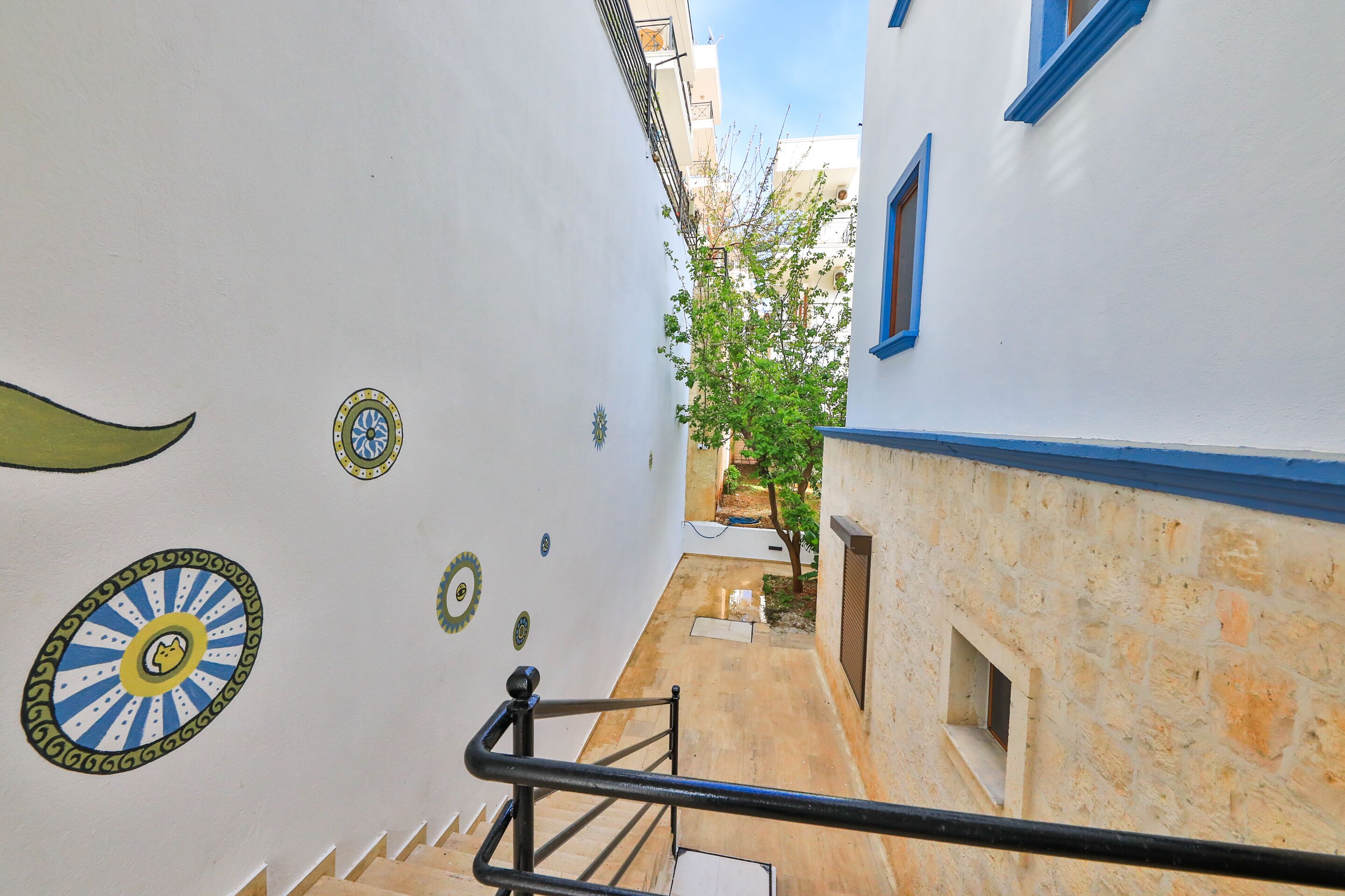 Un callejón estrecho con una escalera que conduce a un edificio con detalles azules y un árbol al fondo.