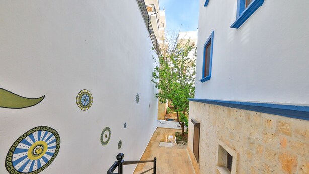 Une ruelle étroite avec un escalier menant à un immeuble aux ornements bleus, et un arbre en arrière-plan.