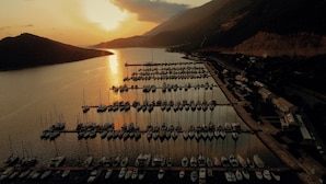 Un port de plaisance où de nombreux bateaux sont amarrés, entouré de montagnes et illuminé par un coucher de soleil.