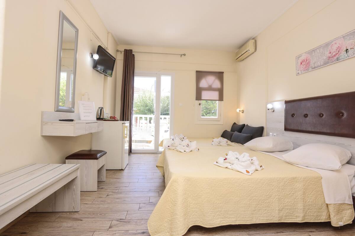A hotel room with a bed, a bench, a TV, and a window with curtains.