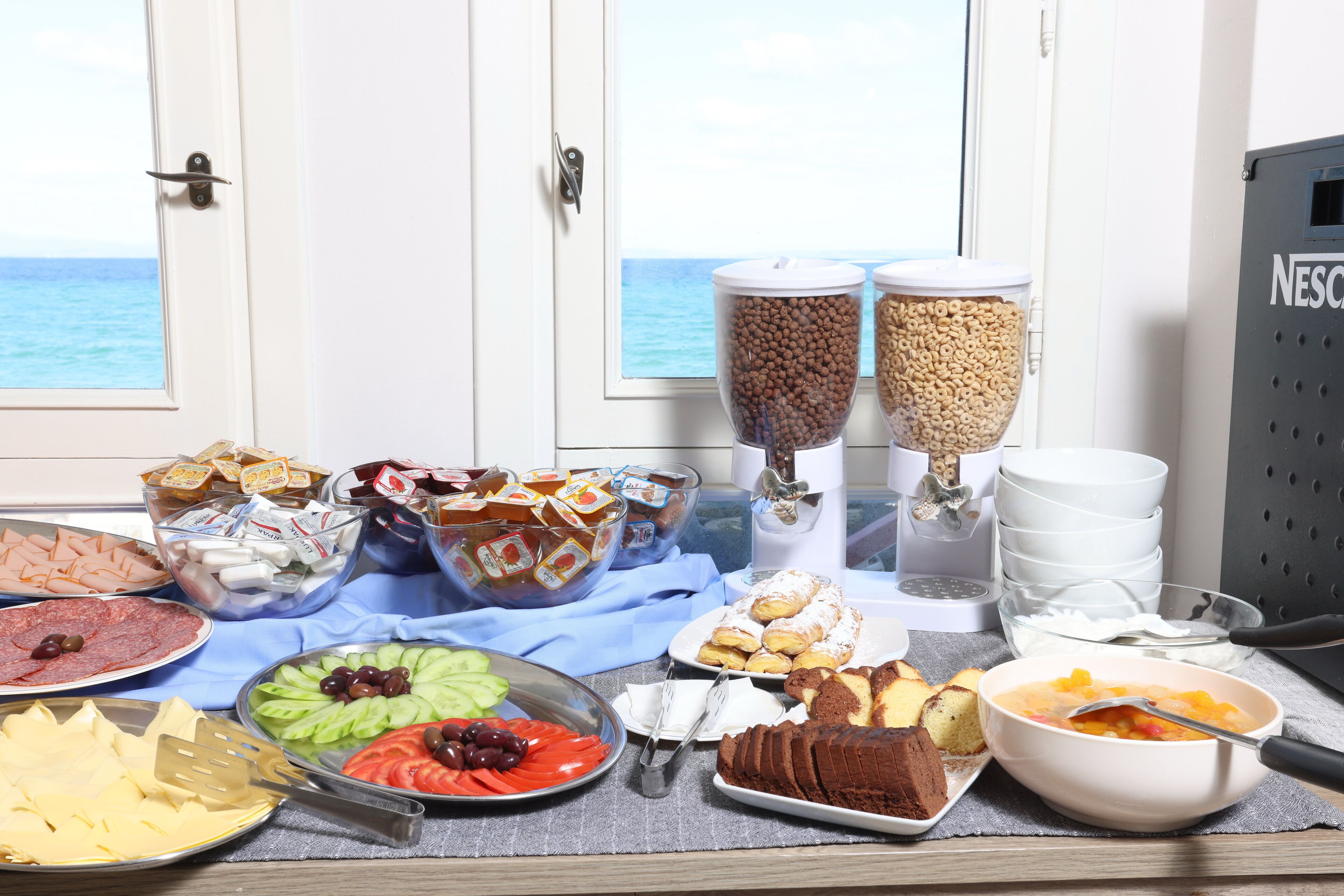 A buffet table with various food items and a view of the sea through a window.