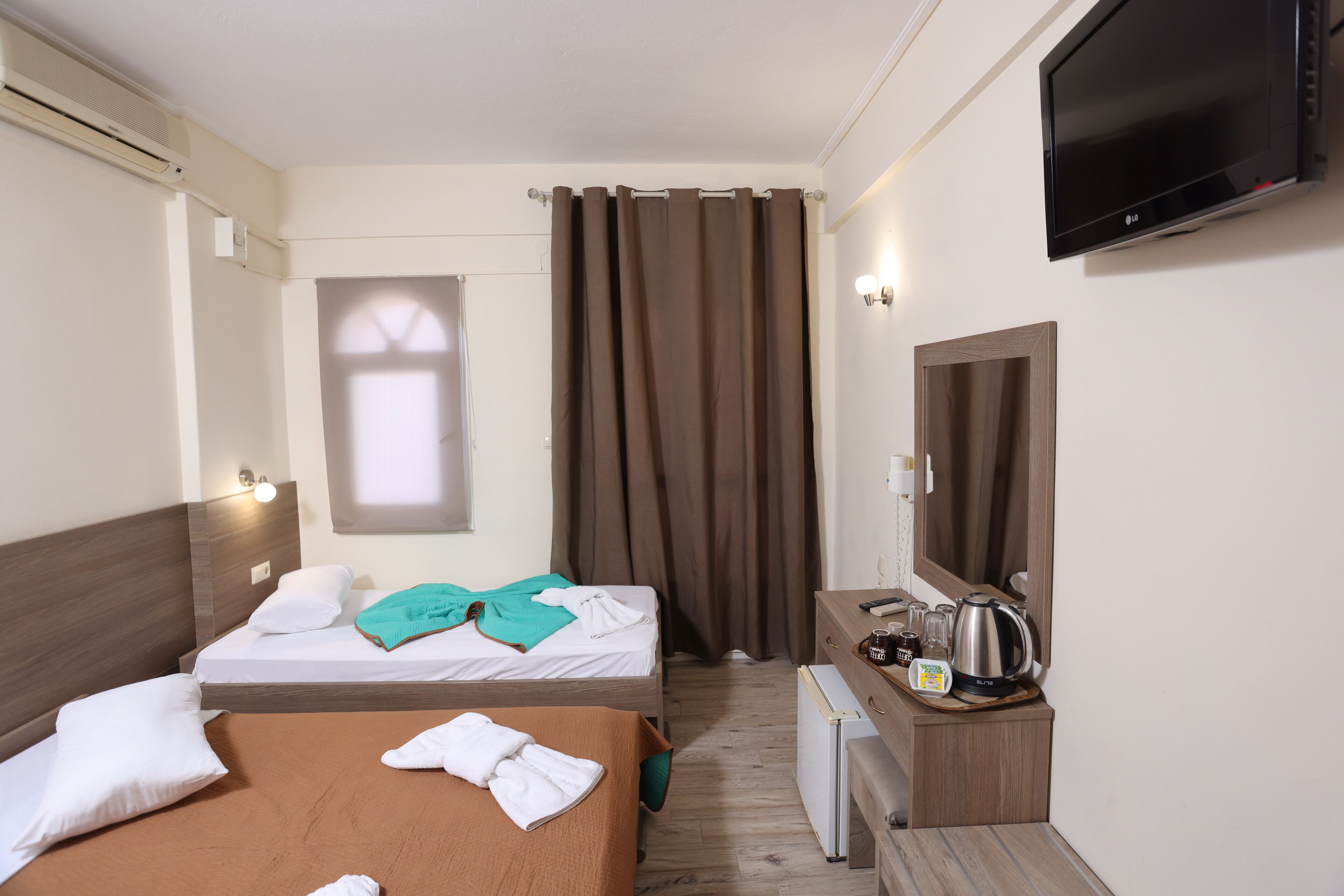 Camera d'albergo con due letti, televisione, angolo cottura e finestra con tende.
