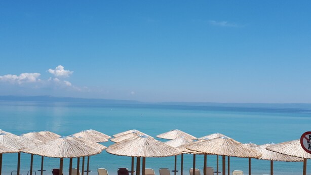 A beach with rows of sun loungers and thatched umbrellas, overlooking a calm sea. - Summer Beach Hotel (Kassandra)