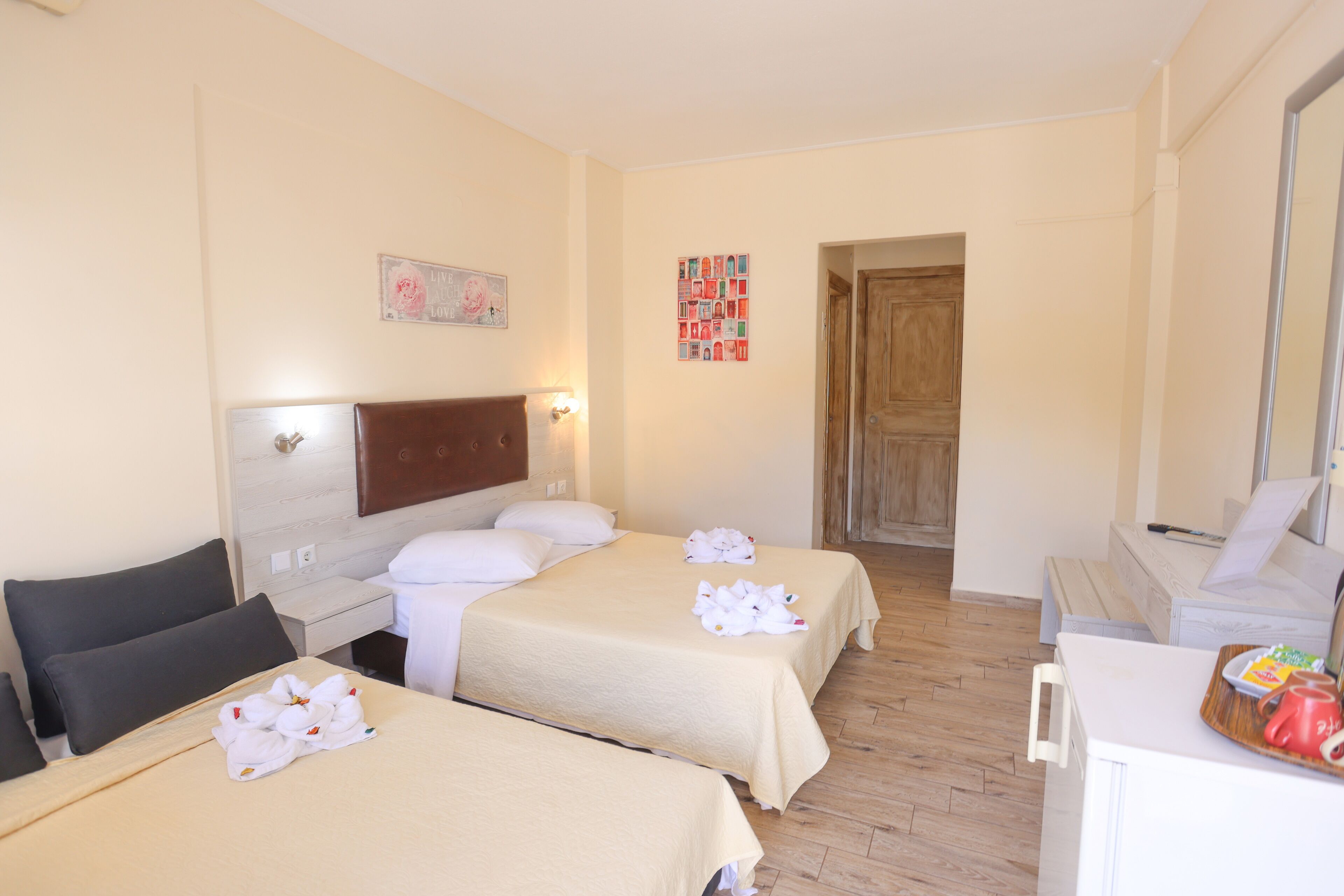 Una camera d'albergo con due letti, una testiera in legno, una scrivania e un'area pranzo con un vassoio di cibo.
