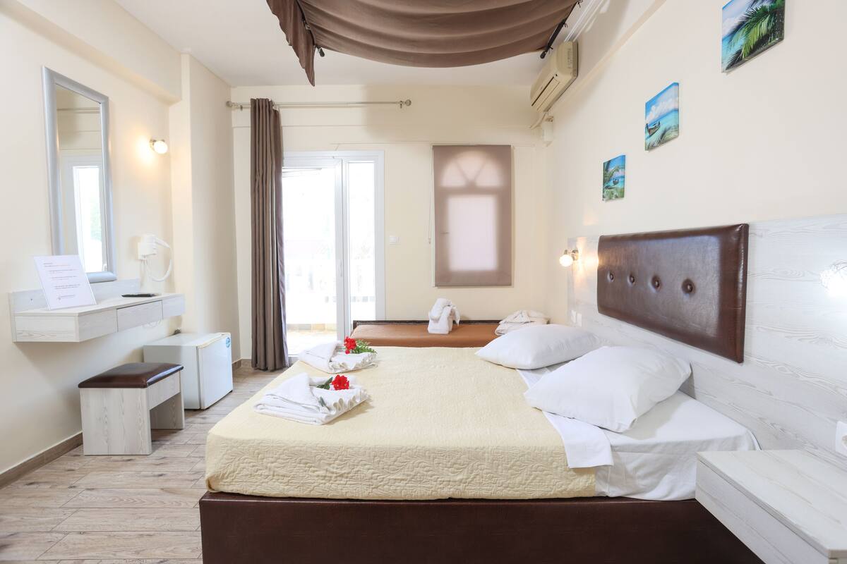 A hotel room with a bed, bedside table, mirror, and a view of the outside.