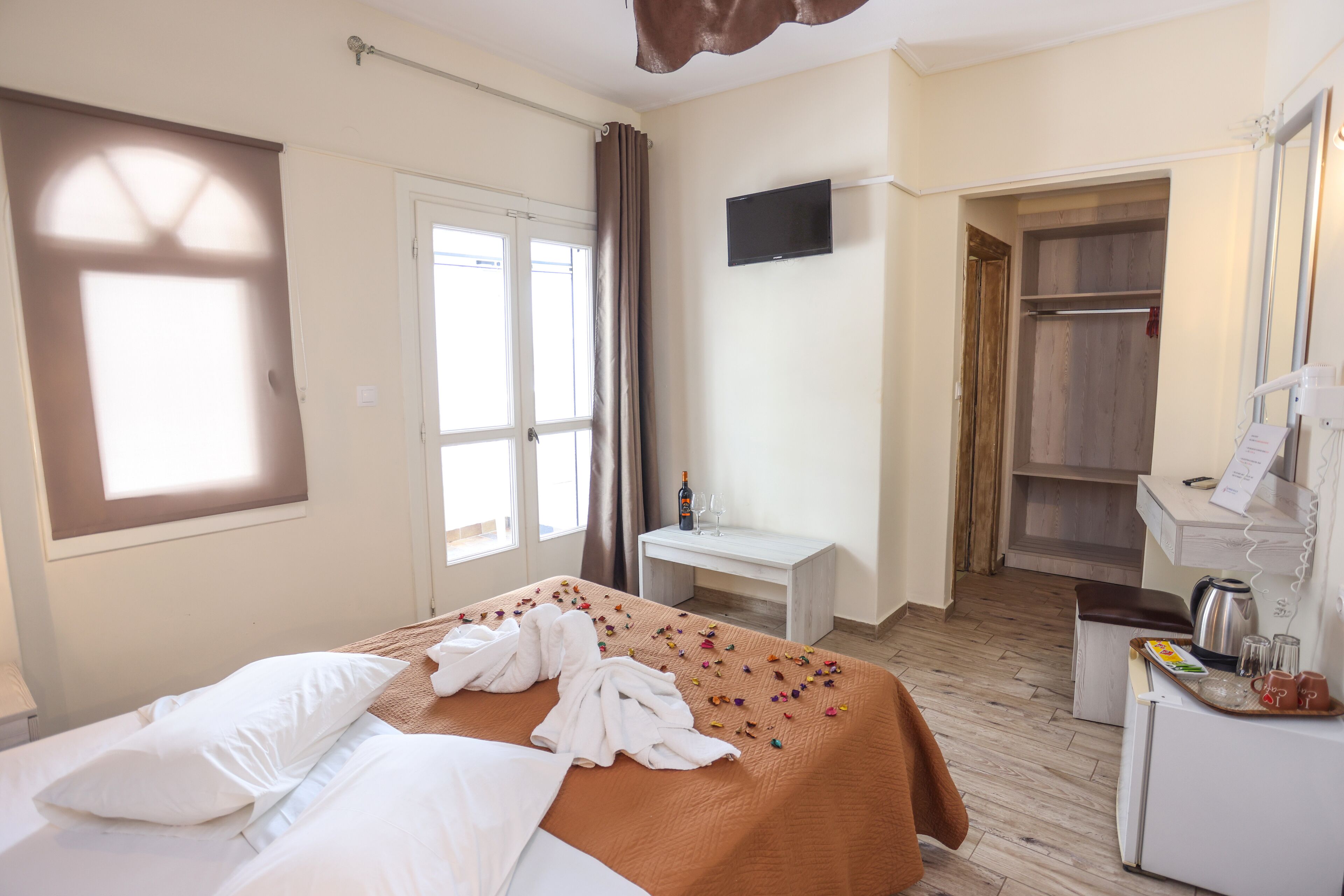 Habitación de hotel con cama, una mesita con una botella y vasos, un televisor en la pared y un armario.