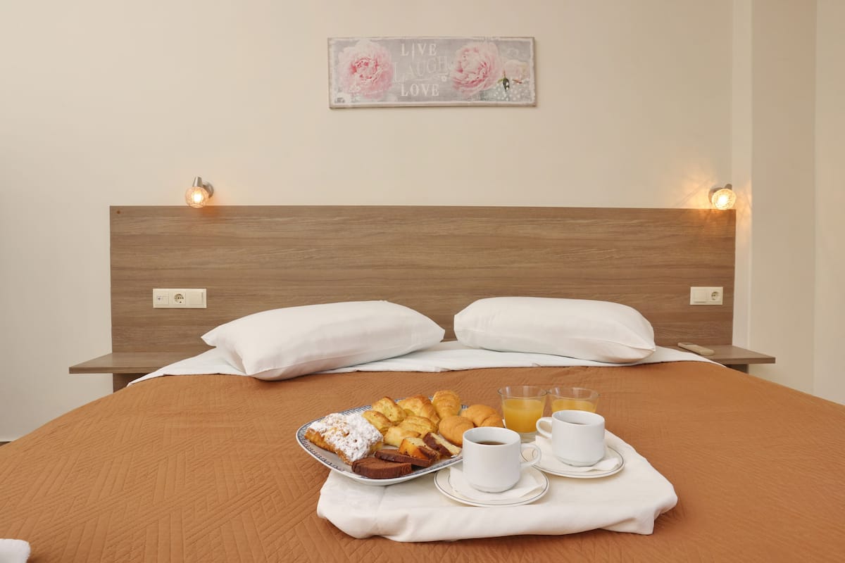 A neatly made bed with a wooden headboard, white pillows, and a breakfast tray with pastries, coffee, and juice.