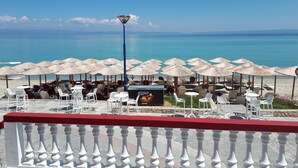 A seaside restaurant with outdoor seating, a view of the sea, and a red railing. - Summer Beach Hotel (Kassandra)
