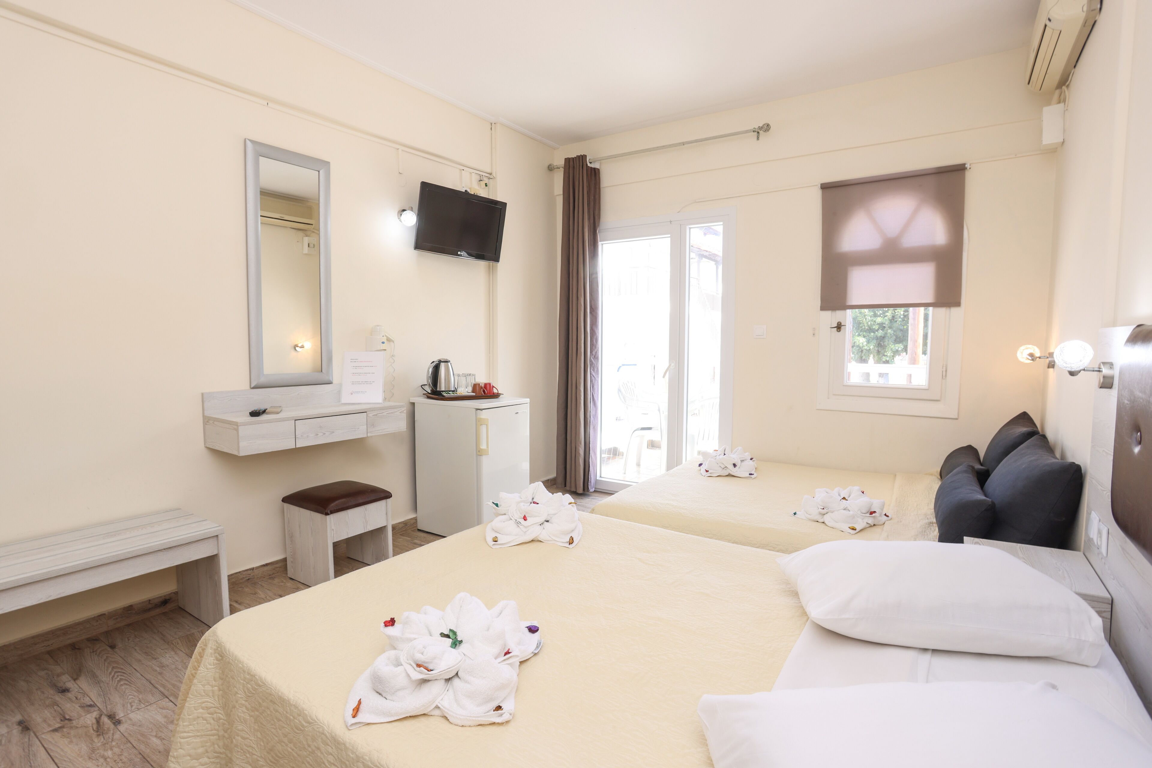 Habitación de hotel con dos camas, un escritorio, un espejo, un televisor y una ventana con cortinas.