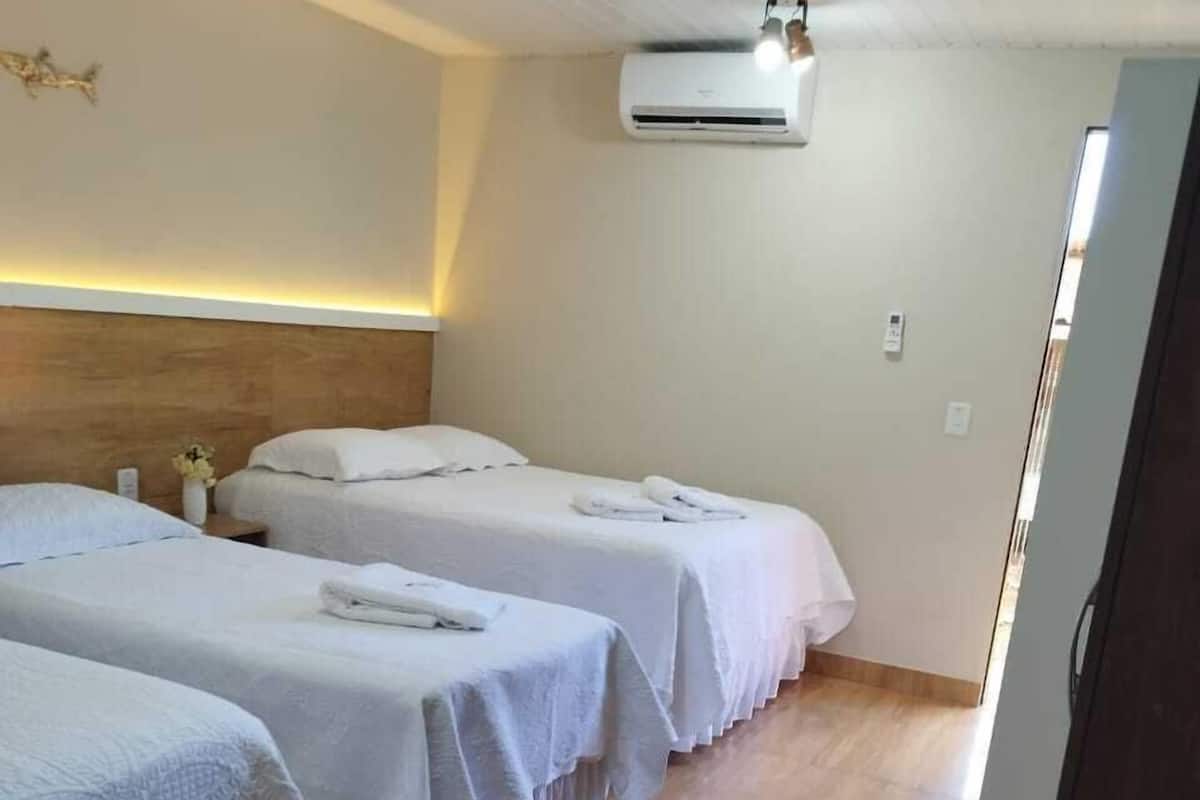 Ein Hotelzimmer mit drei Einzelbetten, Holzboden, Klimaanlage und einem Holz-Kopfteil.