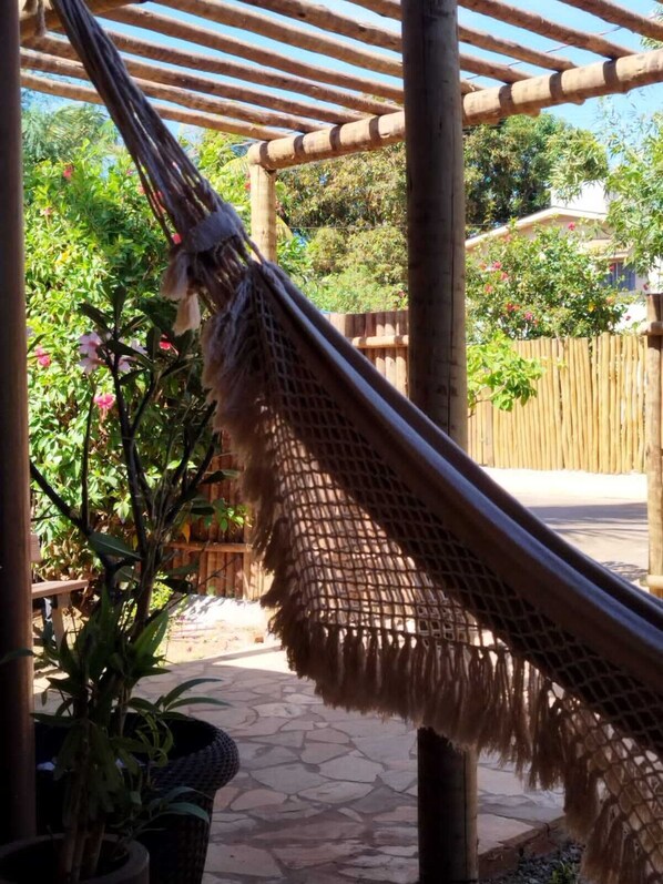 A hammock hanging between bamboo poles in a garden area with potted plants and a wooden fence.