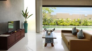 A modern living room with a flat-screen TV, a coffee table, a sofa, and a view of a pool and greenery. - The Miracle Villas Nusa Dua (Nusa Dua)