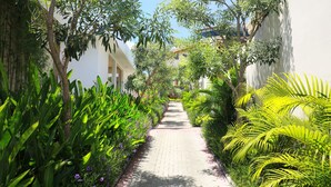 A pathway flanked by lush greenery and white buildings, leading to a building with a red roof. - The Miracle Villas Nusa Dua (Nusa Dua)