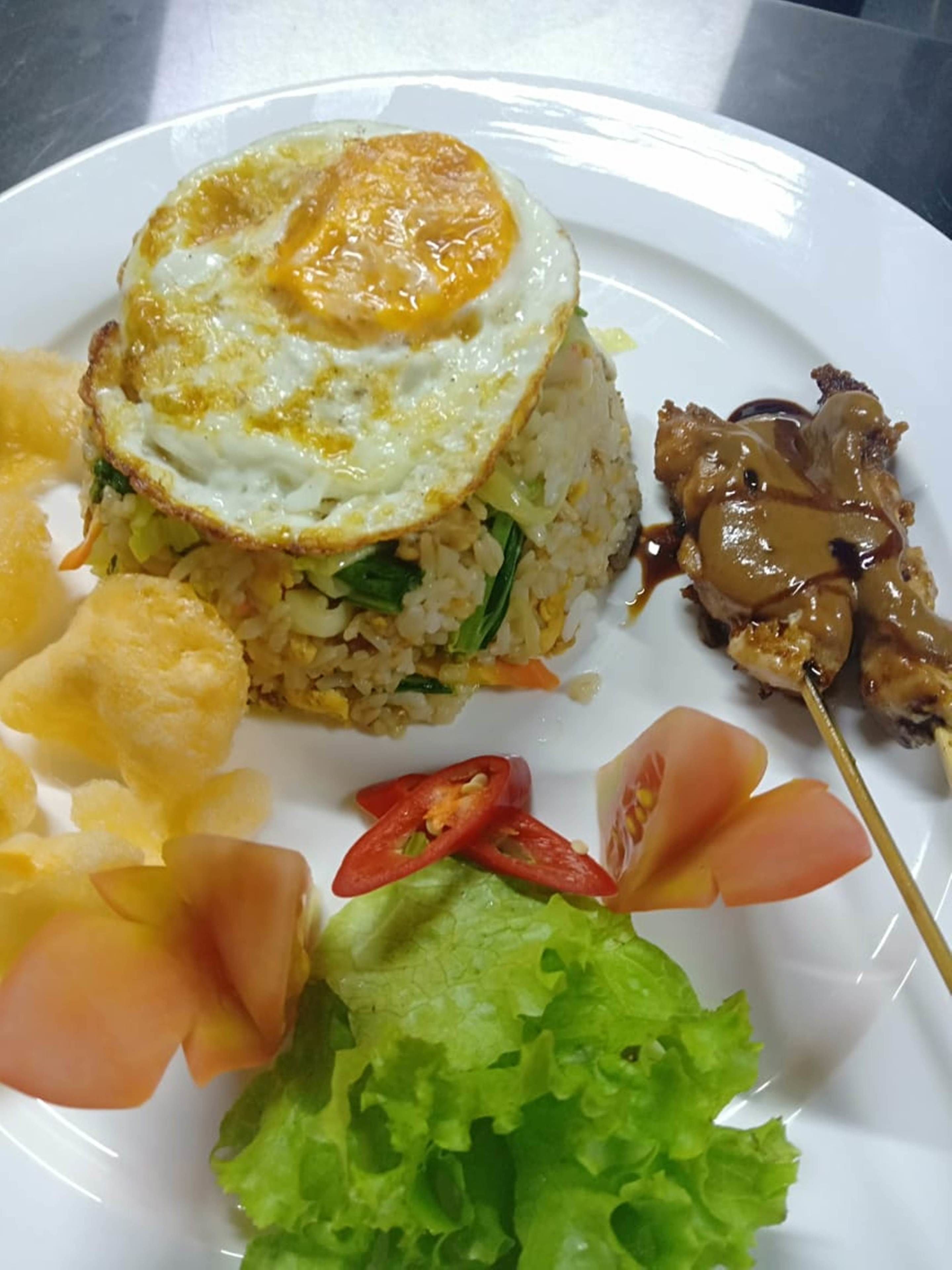 Un plato de arroz frito con huevo, acompañado de verduras y una porción pequeña de carne.