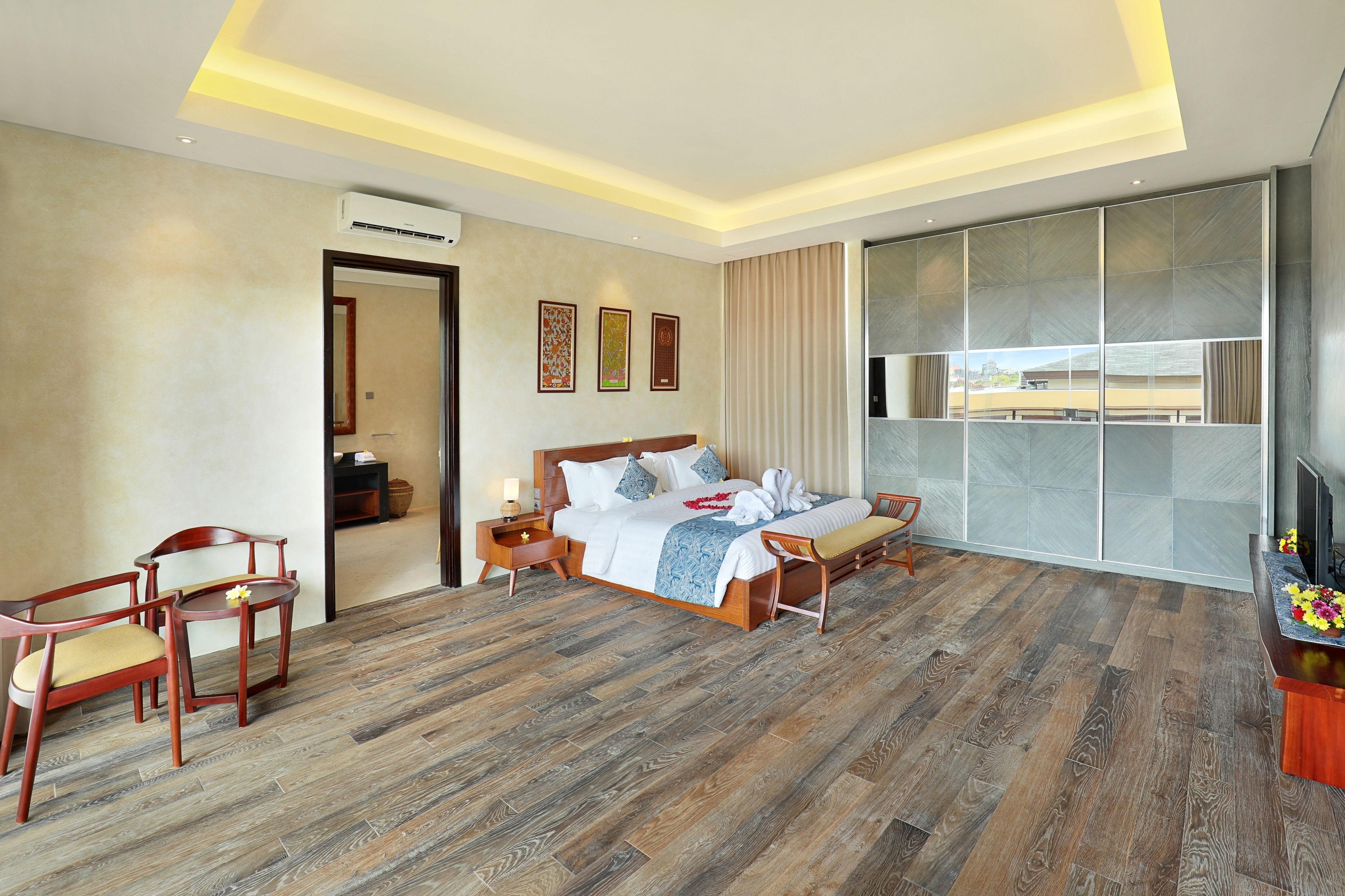 A modern hotel room with a wooden floor, a large bed with a wooden headboard, a desk with a chair, a TV, and a large window with a view.