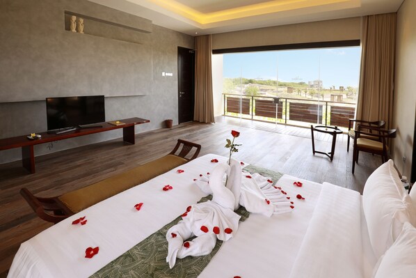 A hotel room with a large bed, a TV, a balcony with a view, and a dining area.