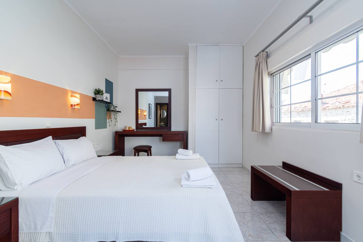 Ein Hotelzimmer mit einem großen Bett, einem Schreibtisch, einem Spiegel, einem Kleiderschrank und einem Fenster mit Vorhängen.