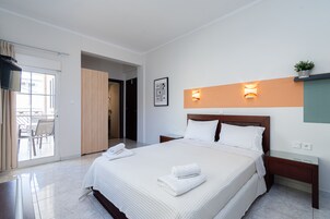 A modern hotel room with a large bed, a bedside table, a nightstand, a wall-mounted TV, and a sliding door leading to a balcony.