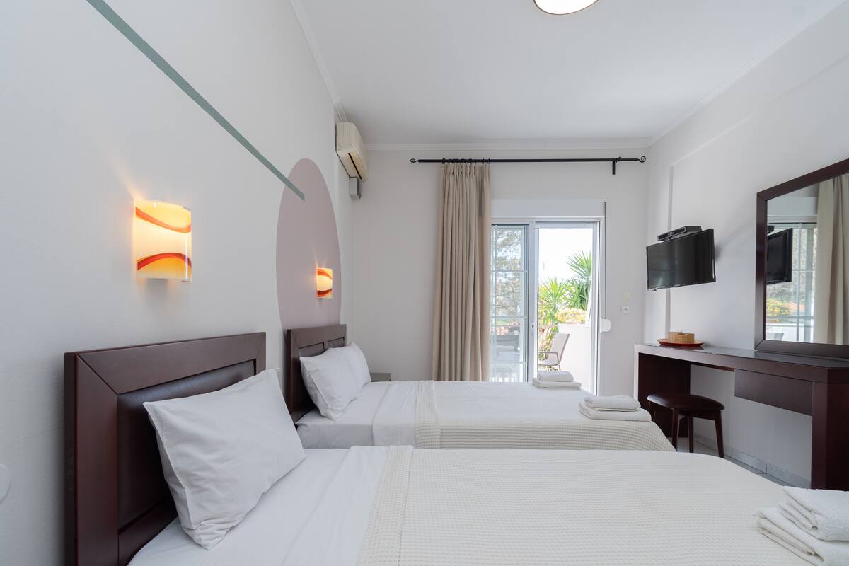 Ein Hotelzimmer mit zwei Betten, einem Fernseher, einem Schreibtisch und einem Fenster mit Vorhängen.